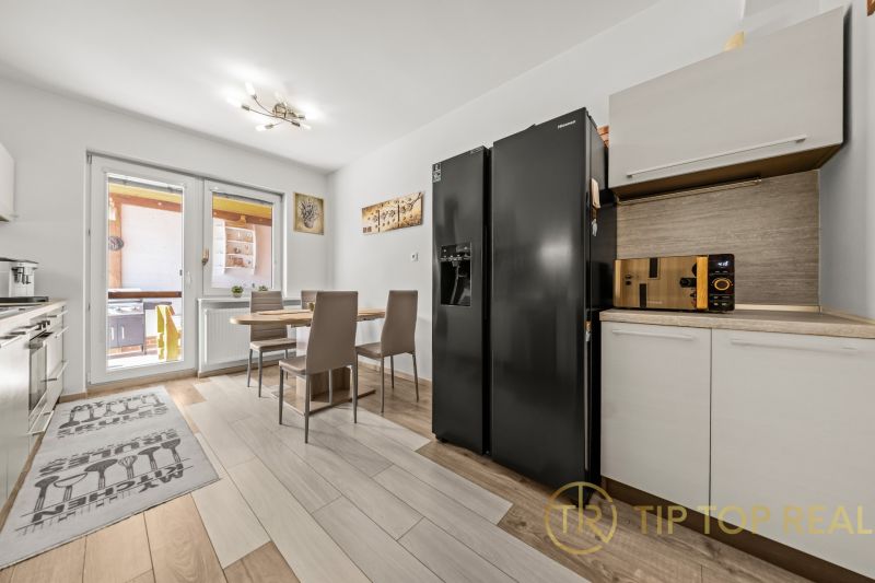 A kitchen in a family house with a refrigerator, a dining table, and a floor with a wooden decor.