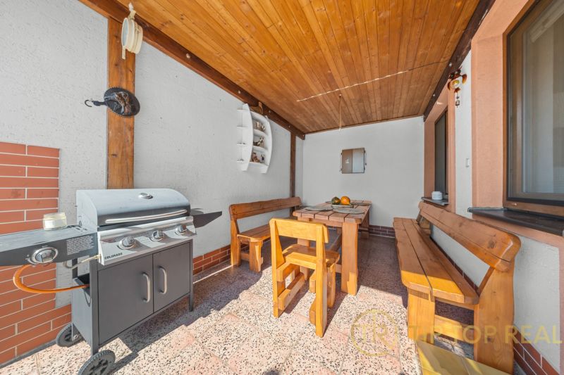 A terrace with a grill and wooden seating at a family house, wooden ceiling, bricks on the wall.