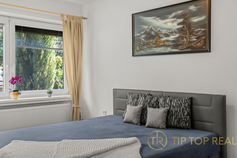 A bedroom in a family house with a painting, a bed, and a view of the garden.