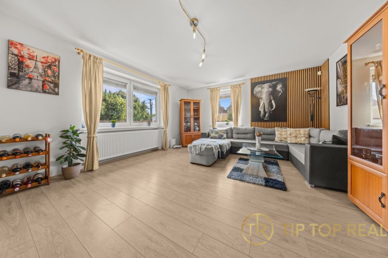 Living room in a family house with a wooden decor floor, a corner sofa, and decorations.