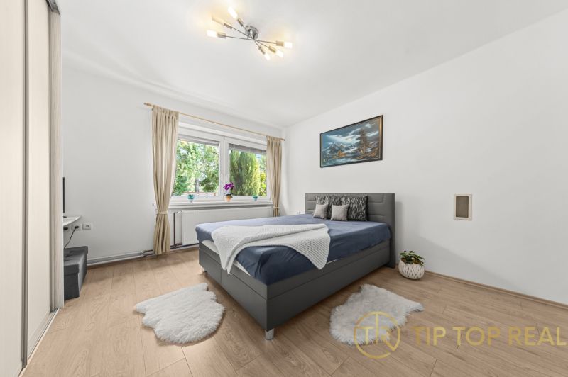 A bright bedroom with a bed, a painting, and a wooden decor floor in a family house.