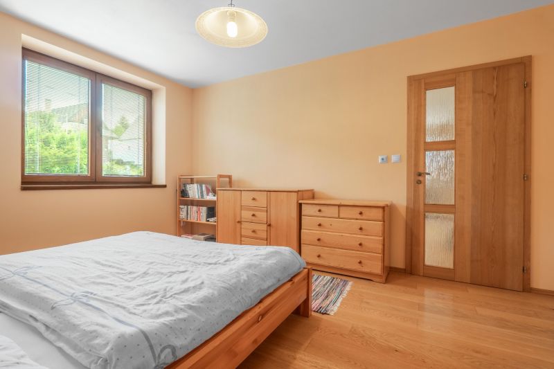 A bedroom in a family house with a bed, dressers, and a floor with a wood decor.