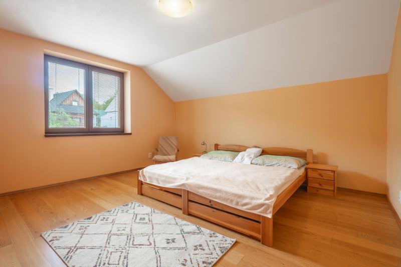 Bedroom with wood-patterned flooring in a family house, light furniture, and a window with a view.