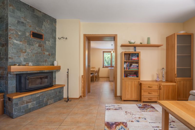 A fireplace with a stone cladding in the living room of a family house with wooden furniture and tiles.