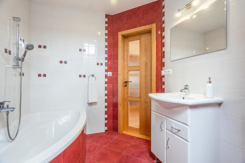 A bathroom in a family house with white and red tiles and a corner bathtub.