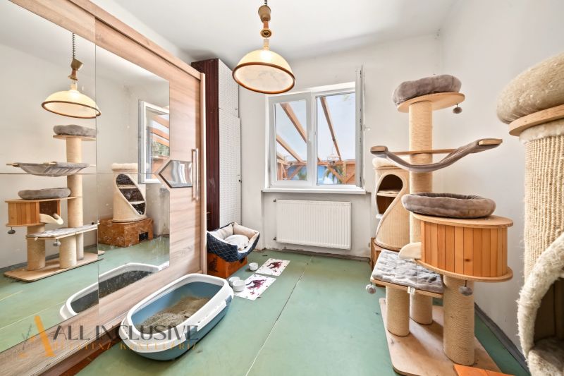 A room in a family house with a cat tree, a mirrored wardrobe, and a floor with a wooden decor.