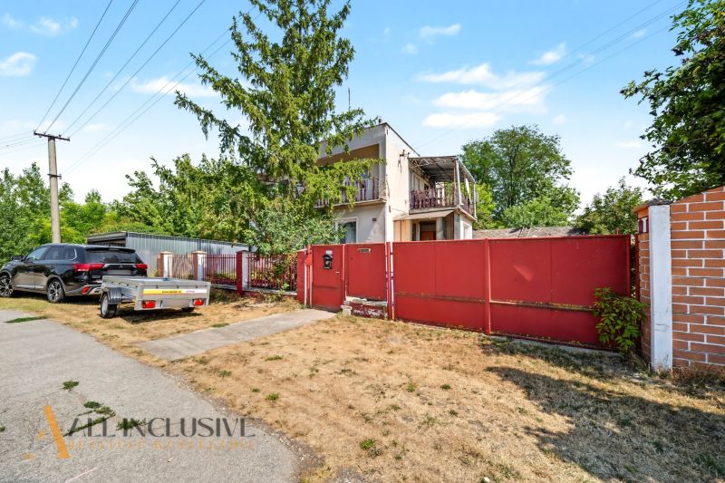 A family house in Bodza with a garden, a car, and a trailer by the road.