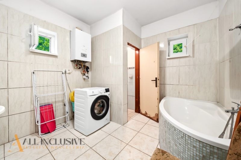 A bathroom in a family house with a washing machine, a corner bathtub, and a gas boiler.