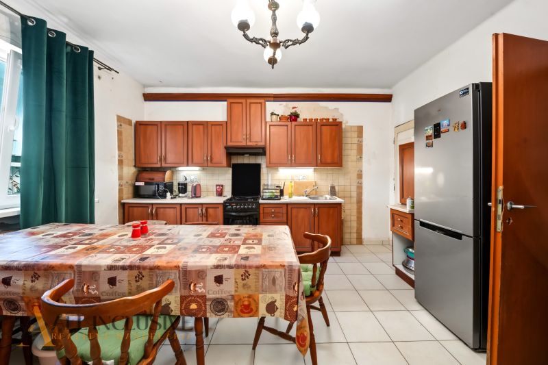 A kitchen in a family house with a dining table, wooden cabinets, and a refrigerator.