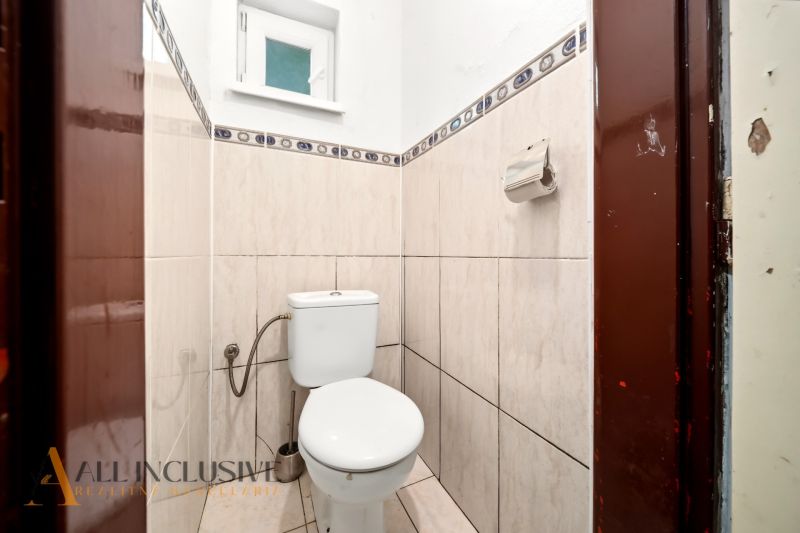 A small bathroom with a toilet, tiled with light tiles, with a window and a paper holder.