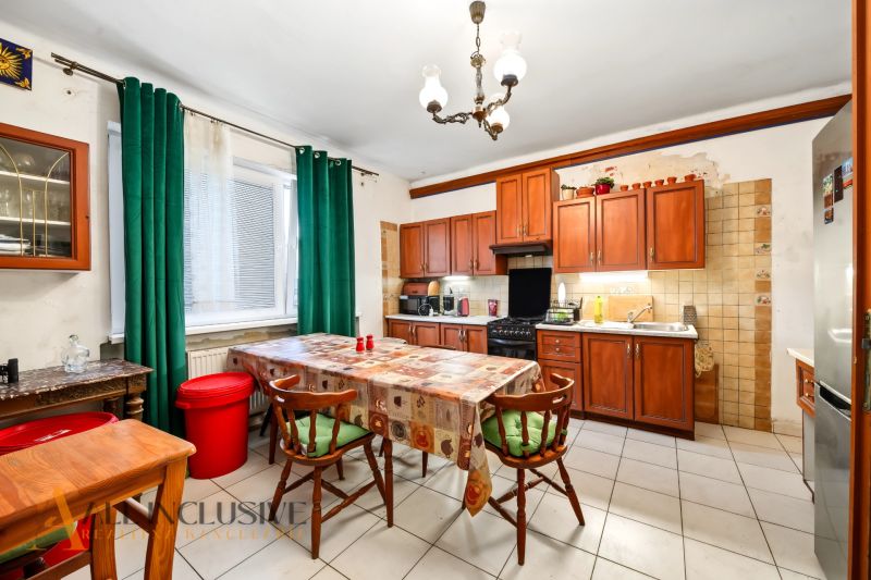 A kitchen in a family house with wooden cabinets, a dining table, and green curtains.
