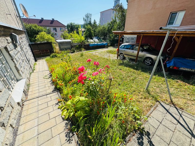 Flower beds by the road in Krupina, next to a 2-room apartment, car parked under a shelter.