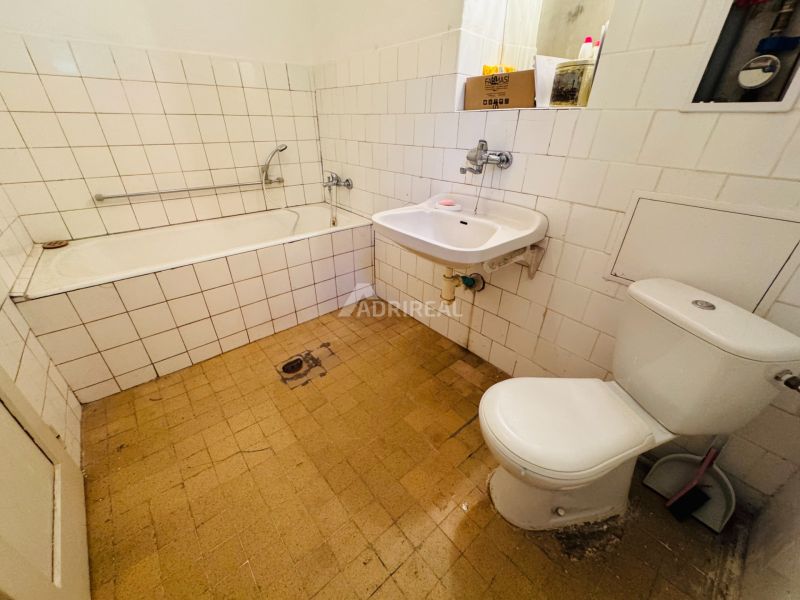 A bathroom in a 2-room apartment with a bathtub, sink, and toilet, tiled with white tiles.