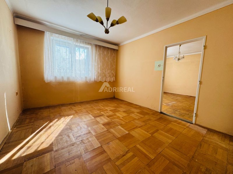 A room in a 2-room apartment with a wood-patterned floor and curtains on the window.