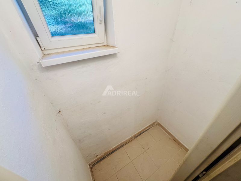 A small room with a window, white walls, and light tiles in a 2-room apartment.