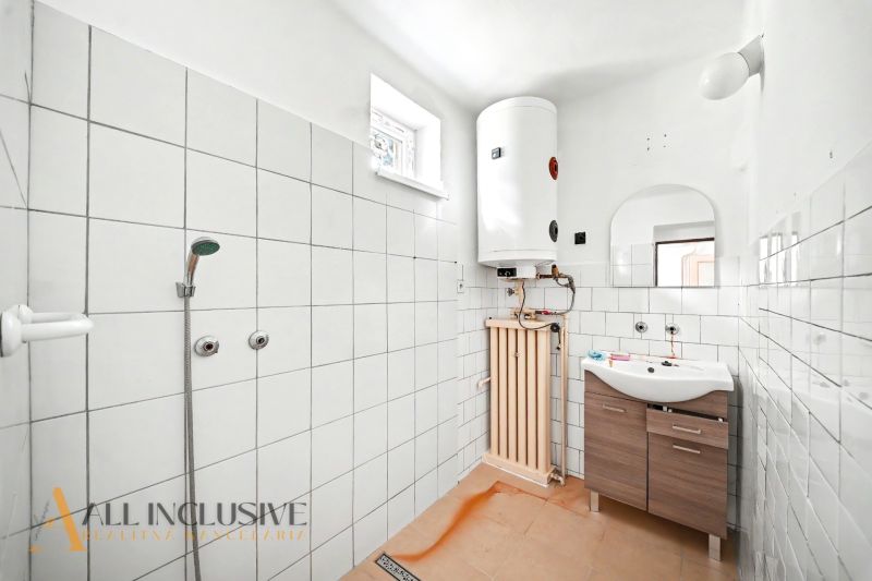 A bathroom in a family house with tiles, a shower, a boiler, and a sink with a wood-like finish.