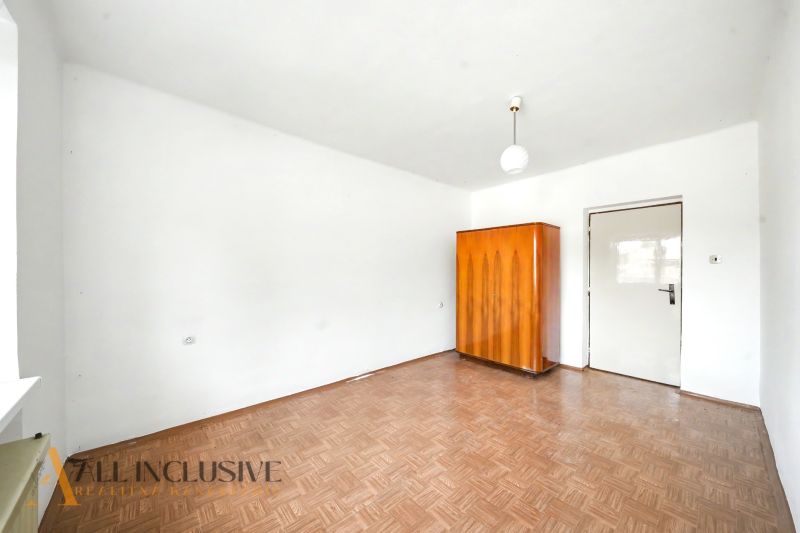 A room in a family house with white walls, a wooden decor floor, and a wooden wardrobe.