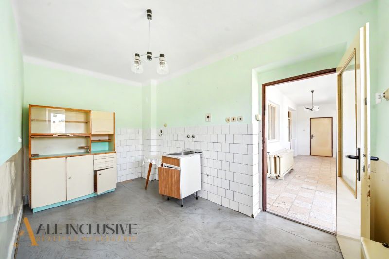 A kitchen in a family house with a simple kitchen unit, white tiles, and a gray floor.