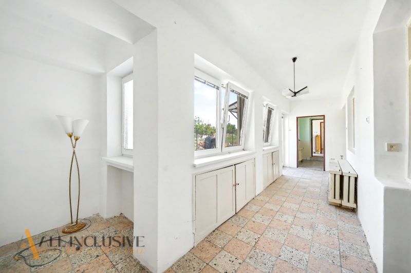 A hallway in a family house with large windows, tiled flooring, and a light fixture.