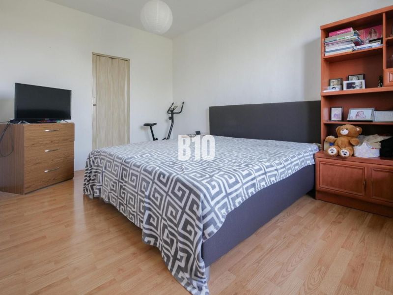 Bedroom in a two-room apartment with a wood-patterned floor, bed, and shelf.