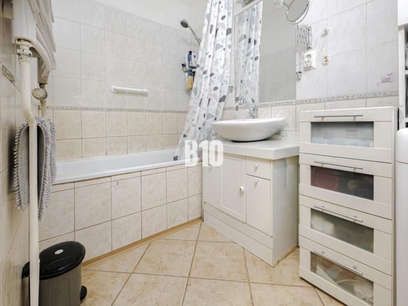 A bathroom in a 2-room apartment with a bathtub and a white sink on a cabinet.