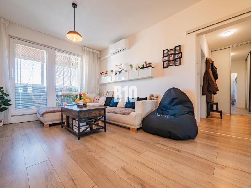 Living room in a 3-room apartment with a wooden decor floor, a sofa, and large windows.