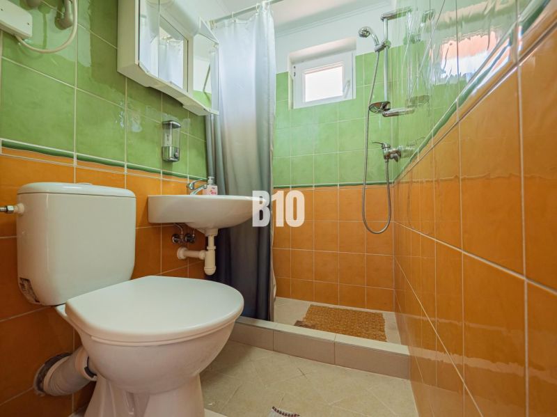 A bathroom in a family house with orange and green tiles and a shower corner.
