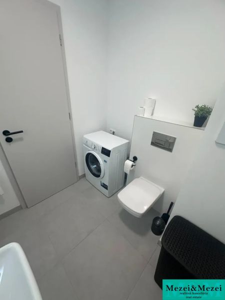 Bathroom with a washing machine, toilet, and beige tiles in a 2-room apartment.