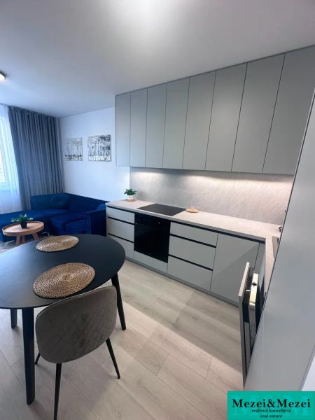 Kitchen corner with a cooktop, round table, sofa, wooden decor flooring.
