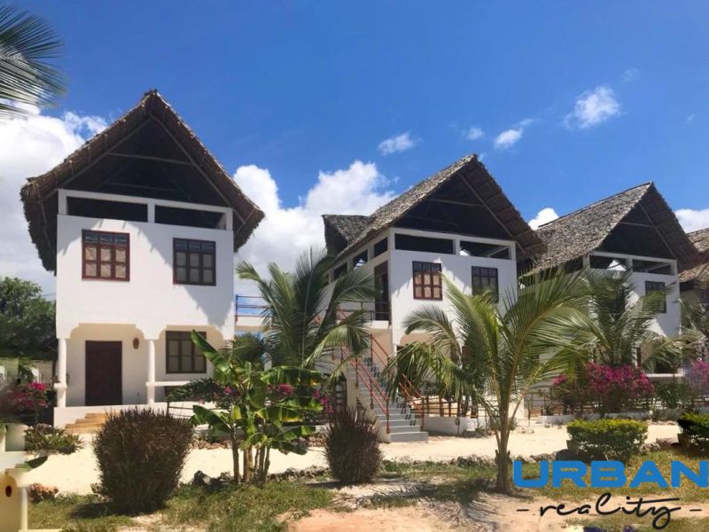 A family house in Fumba Town with palm trees and a thatched roof under a blue sky.