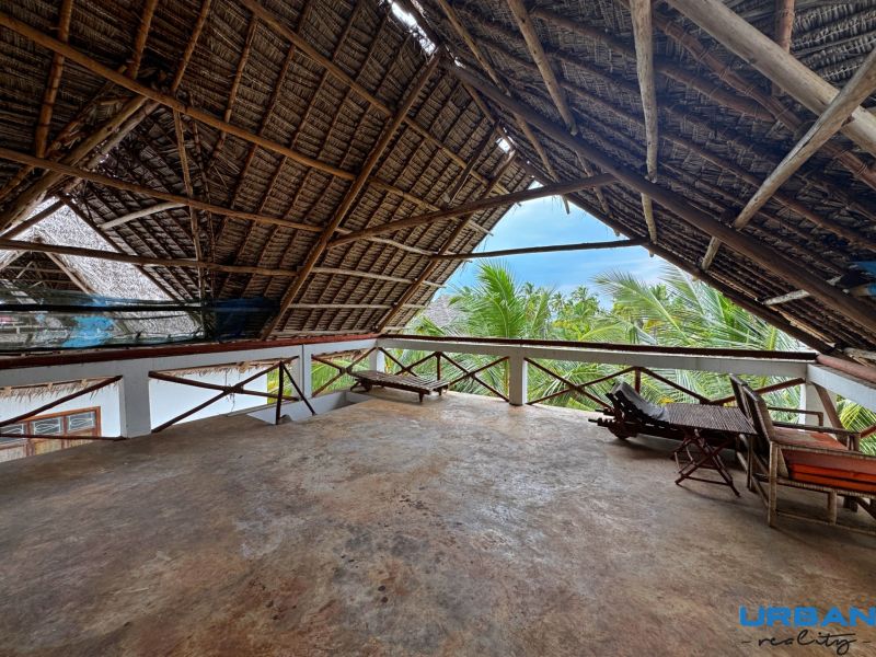 Rustic roof on the upper floor of a family house in Fumba Town with a view of palm trees.