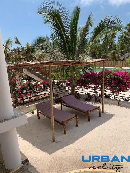 Wooden loungers on the sand with palm trees and flowers in a family house in Fumba Town.