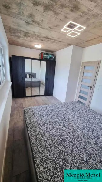 A bedroom in a family house with a wooden decor floor, a mirrored wardrobe, and a bed.