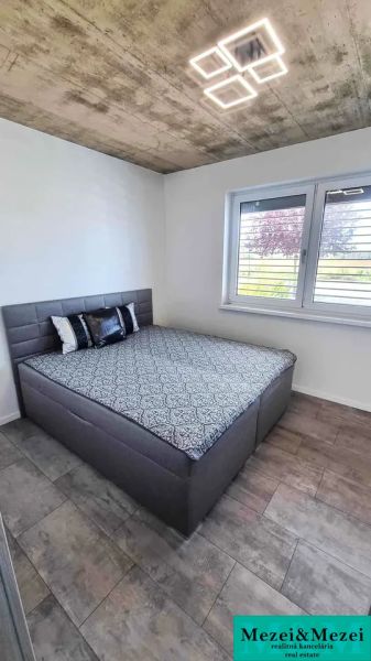 Family house with a bed and floor with wooden decor, simple concrete ceiling.