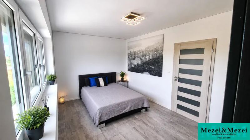 A bedroom in a family house with a large window, a bed, and a wooden decor floor.