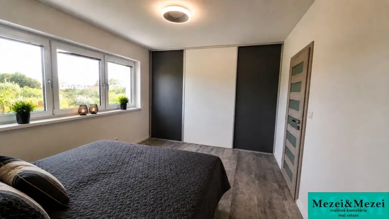 A bedroom in a family house with a large window and a bed, floor with wooden decor.