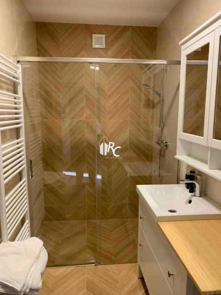 A bathroom with a shower and a floor with a wood decor in a 3-room apartment.