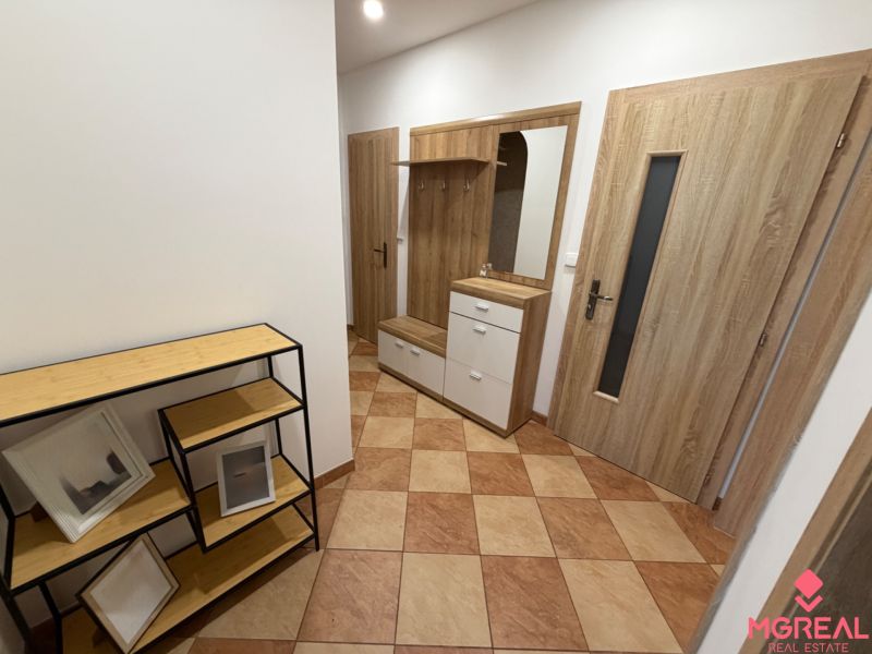 A hallway in a 3-room apartment with tiled flooring, a coat rack wall, and shelves with a wooden decor.