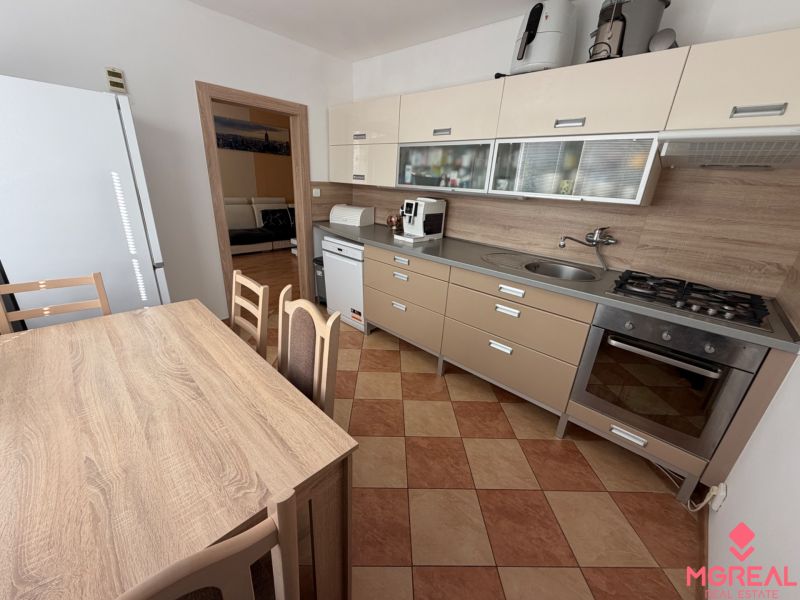 A kitchen of a 3-room apartment with a corner unit, dining table, and appliances.