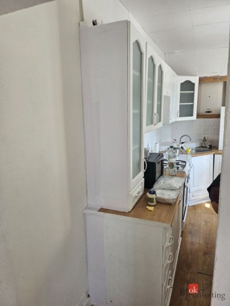A kitchen in a family house with white furniture and a wooden-patterned floor.