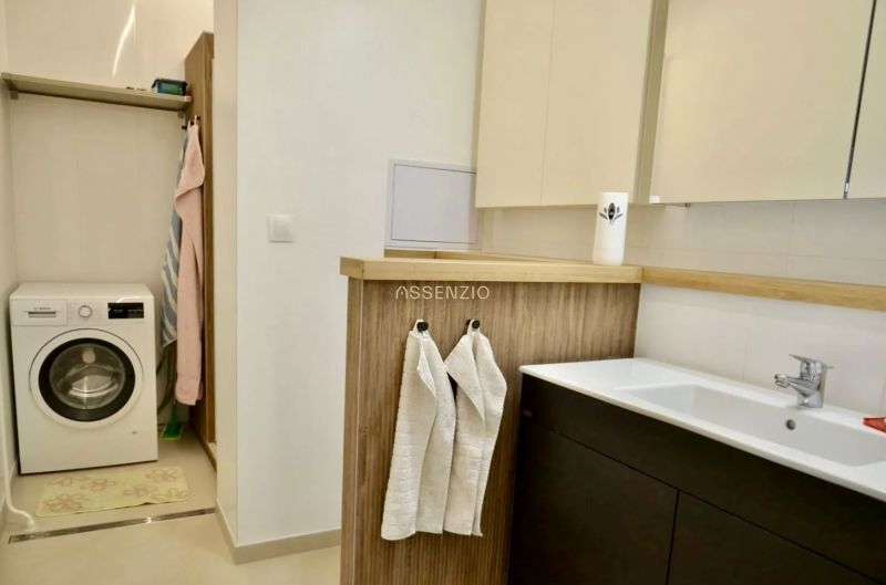 Bathroom in a 3-room apartment with a washing machine, sink, wooden decor, and shelves.