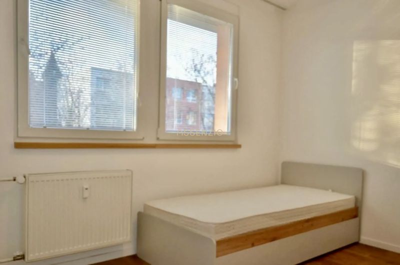 Bedroom in a 3-room apartment with large windows and a wooden decor floor.