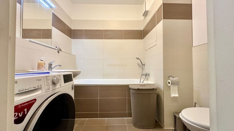 A bathroom in a 3-room apartment with a bathtub, washing machine, and toilet.