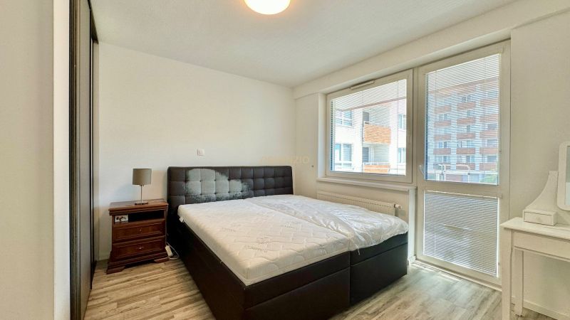 A bedroom in a 3-room apartment with a bed, a nightstand, and a floor with a wooden decor.