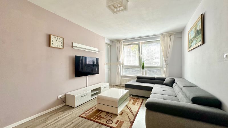 Living room with a corner sofa, TV, coffee table, and floor with wood decor.
