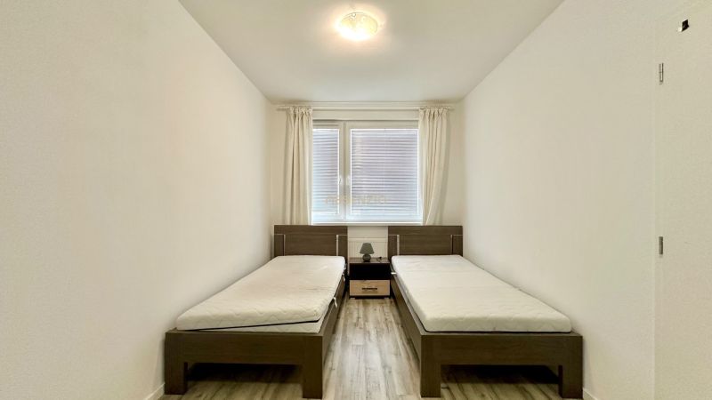 Two single beds, a nightstand, white walls, wood-patterned flooring.