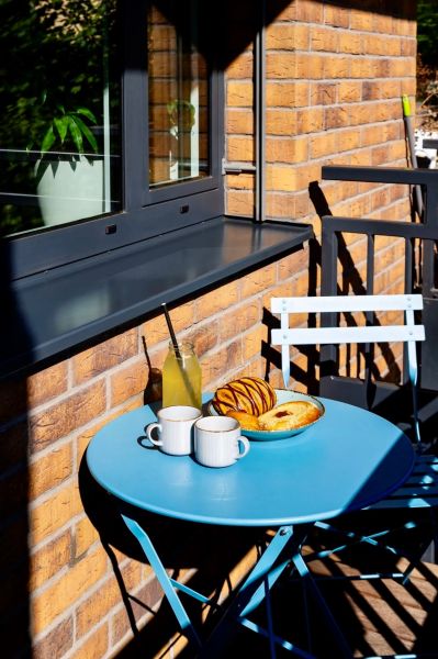 In the 2-room apartment, there is a blue table with cups and pastries on the balcony.
