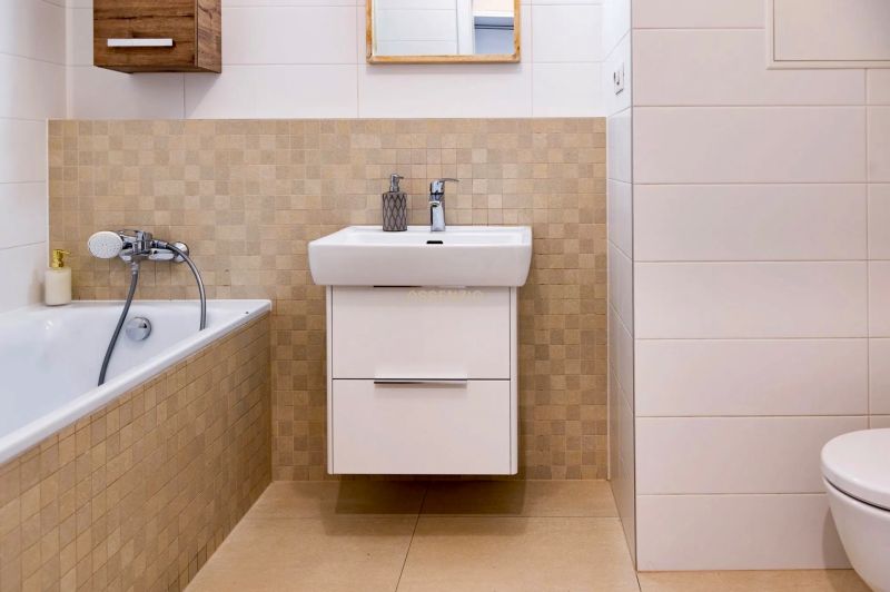 A bathroom with a shower tub, sink, and tiles in a 2-room apartment.