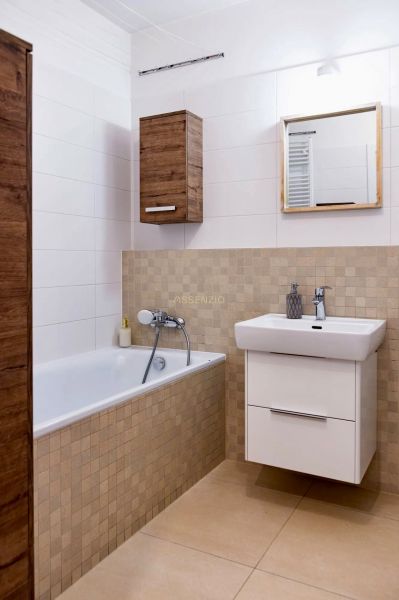 A bathroom in a 2-room apartment with a bathtub, white sink, and wooden decor.