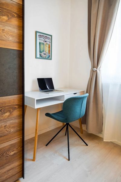 A workspace in a 2-room apartment with a blue chair and a white desk.